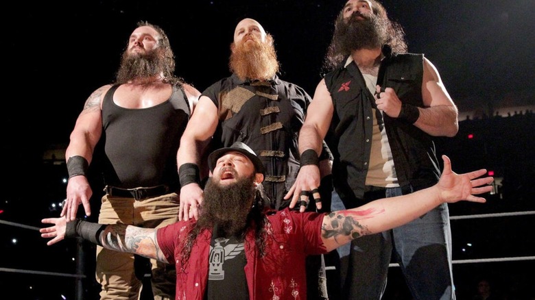 The late Bray Wyatt kneels in front of Braun Strowman, Eric Rowan, and the late Luke Harper in the ring, as the Wyatt Family, on an episode of WWE TV.