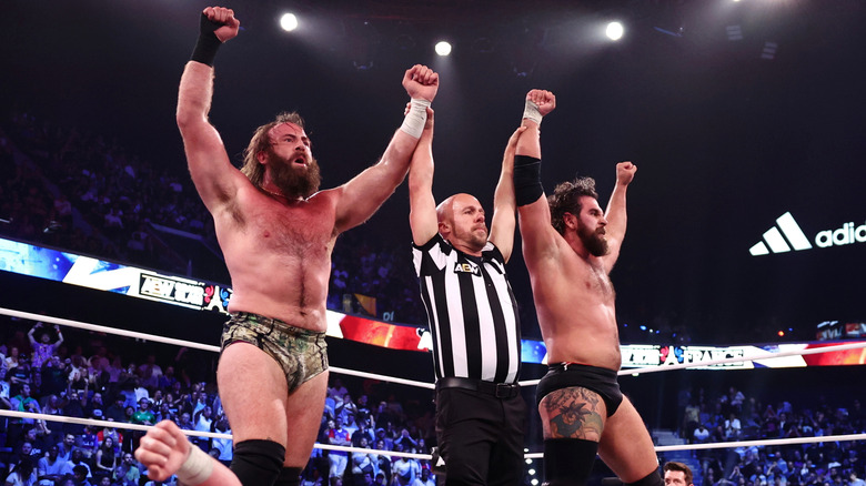 A referee holds up the arms of Mark Davis and Jake Doyle in victory, as they stand over a fallen Gabe Kidd, during the October 6, 2026 edition of 