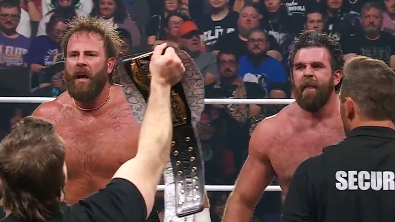 Mark Davis and Jake Doyle stare down Cash Wheeler as he holds up the AEW World Tag Team Championship on the apron following their victory on 