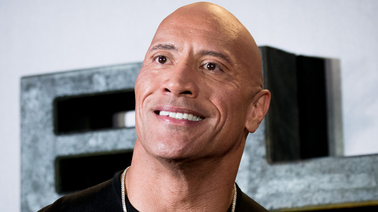 Dwayne "The Rock" Johnson smiling, while people chant "We Want Cody" off-camera