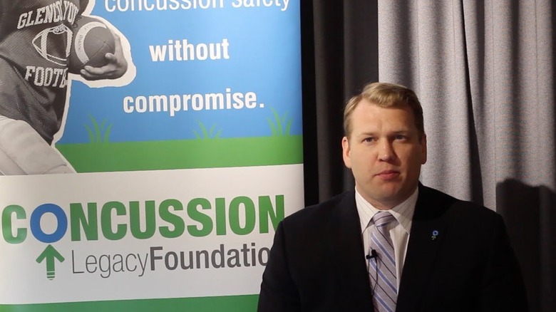 Dr. Chris Nowinski poses in front of a poster promoting his co-founded organization, the Concussion Legacy Foundation