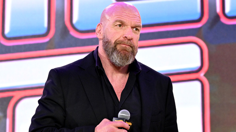 Paul Levesque in an all-black suit holding a microphone
