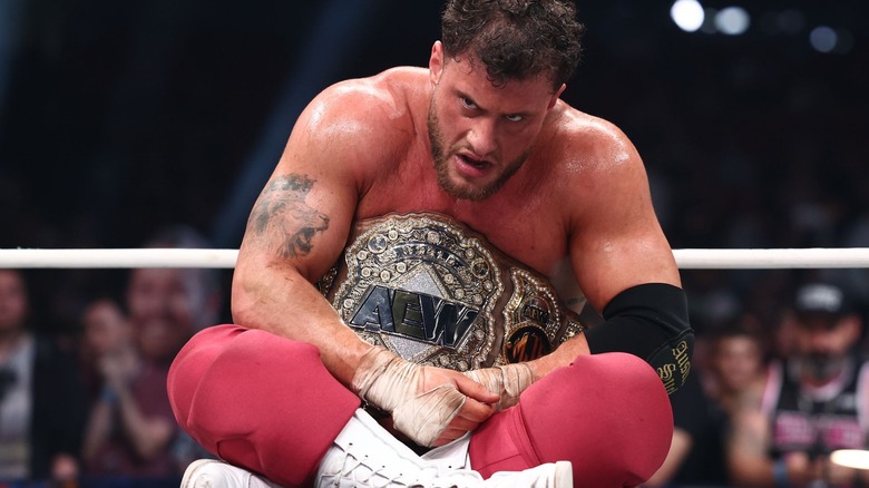 AEW World Champion MJF sits and crouches defensively over his title.