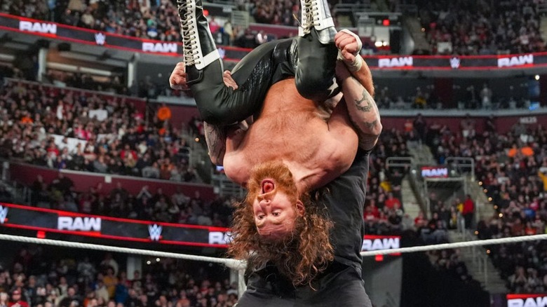Sami Zayn is pictured with a shock expression on his face as he prepares to take a piledriver from Kevin Owens in the ring on an episode of "WWE Raw."