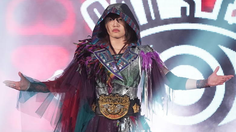Syuri poses at the top of an entrance ramp with the IWGP Women's Championship wrapped around her waist