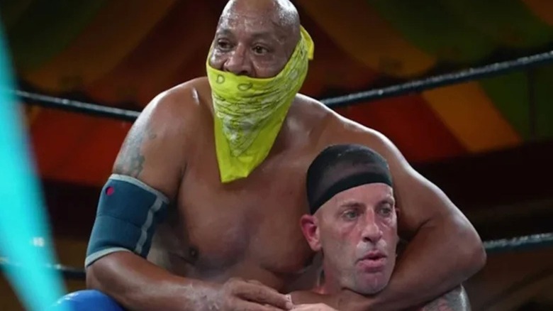 2 Cold Scorpio, seen wearing a yellow bandana across his face, puts an opponent in a hold during a match in GCW.