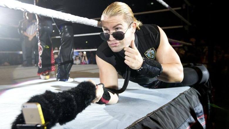 Tyler Breeze poses on the ring apron, dressed as a police officer, taking a photo with a selfie stick, before a match.