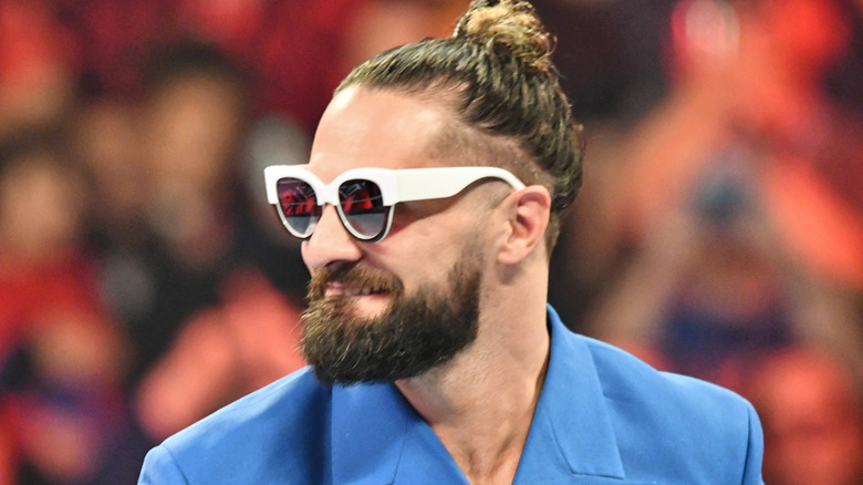 Seth Rollins smiles in WWE ring wearing white sunglasses and light blue jacket