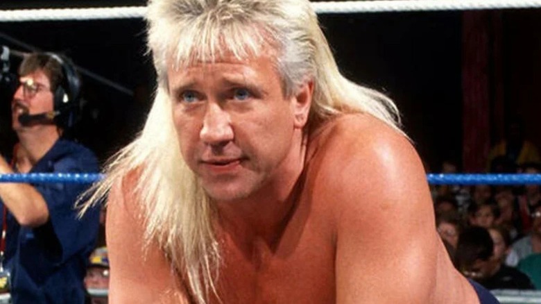 Ricky Morton stares at an opponent while sat in the ring, a cameraman pictured in the background, before a match.