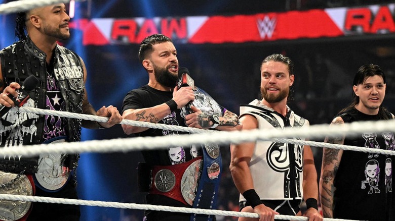 The Judgment Day's Finn Balor cuts a promo on the edge of the ring surrounded by Damian Priest, JD McDonagh, and Dominik Mysterio.