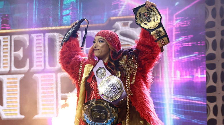 Mercedes Mone holds up some of her championships while wearing others on her way to the ring for a match on AEW programming.