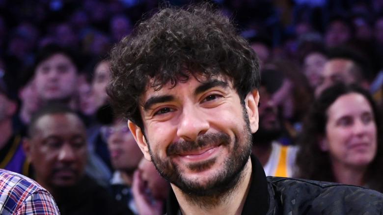 Tony Khan smiles sheepishly with a glass in his hand.