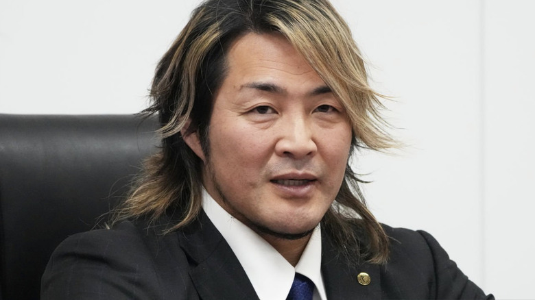 Hiroshi Tanahashi sits at a press conference in a suit and tie.