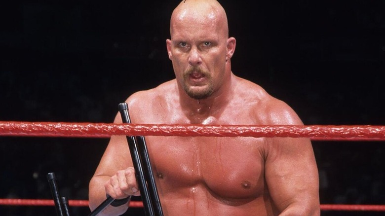 "Stone Cold" Steve Austin kneels in the ring, steel chair in hand, during a match on WWF programming.