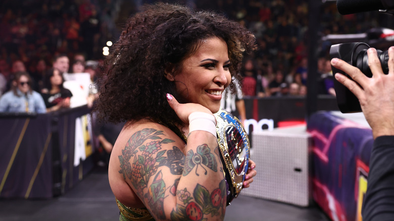 Willow Nightingale is pictured smiling for a camera at ringside, TBS Championship on her shoulder, during an episode of 