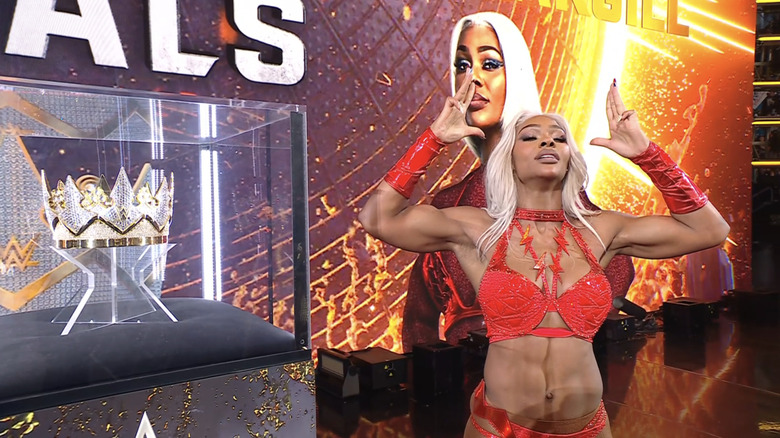 Jade Cargill mimes putting a crown on her head as she stands next to the Queen of the Ring crown.