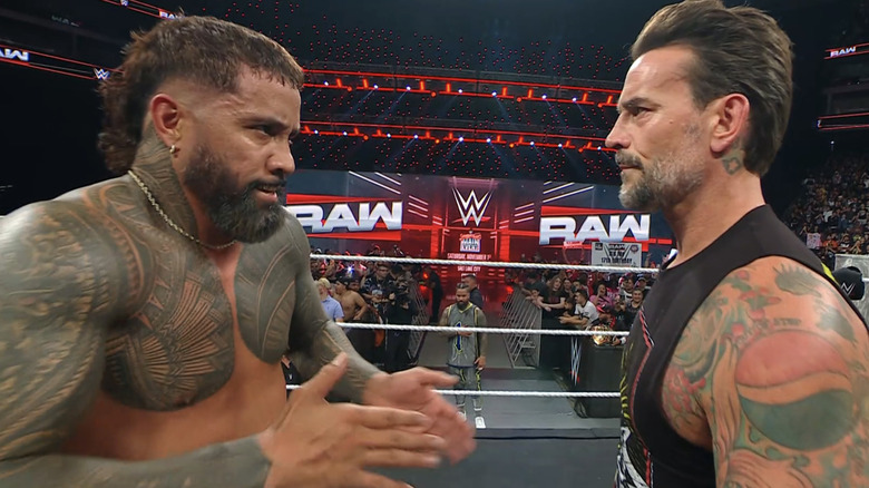 Jey Uso claps his hands together as CM Punk looks on.