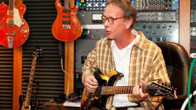 WWE composer Jim Johnston is seen playing the guitar in a studio.