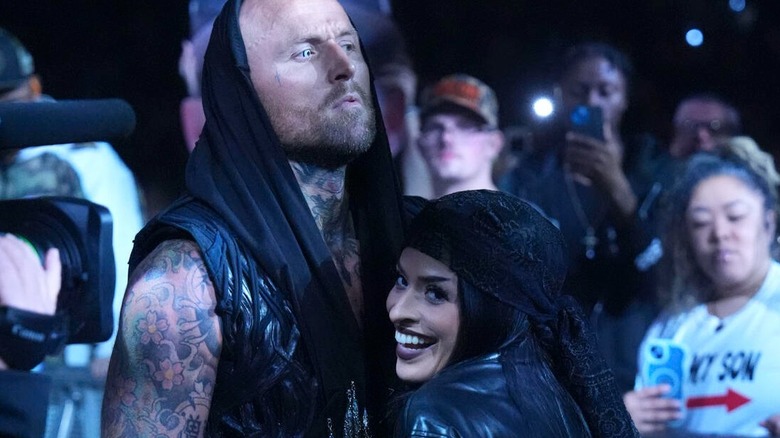 Zelina Vega smiles on towards the camera near the ring while holding real-life husband Aleister Black before his match on "WWE SmackDown"