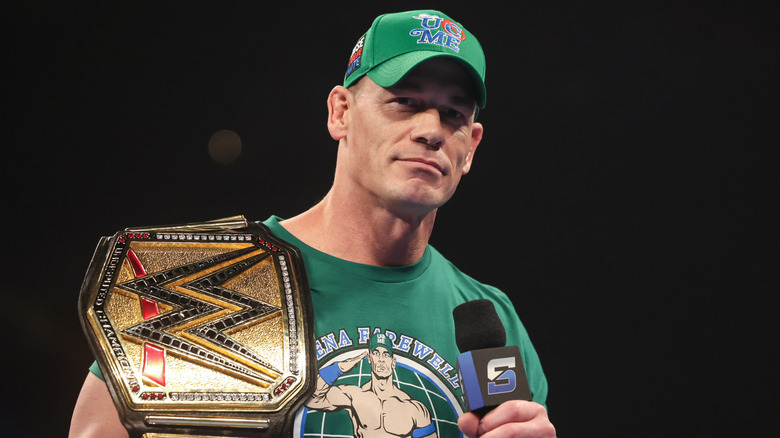John Cena holding a WWE SmackDown microphone with a title on his shoulder
