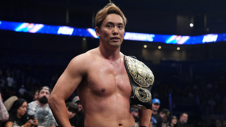 Kazuchika Okada stands ringside with the Unfied Championship on his shoulder after a match on 