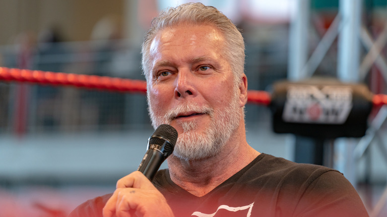 Kevin Nash holding a microphone with ring ropes in the background