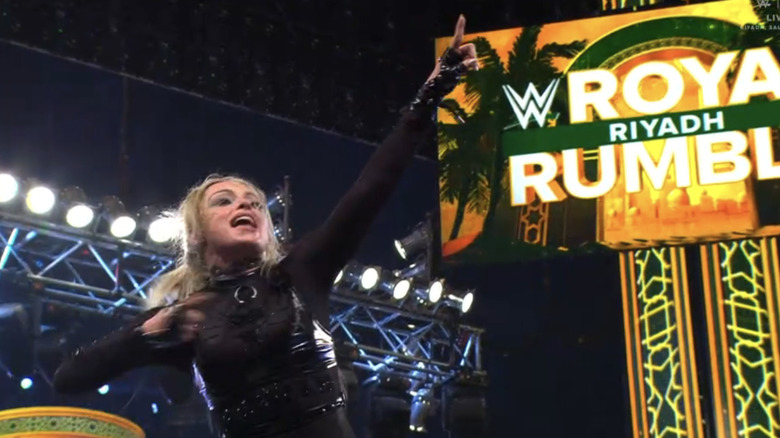 Liv Morgan points to herself and at the offscreen WrestleMania sign, with Riyadh's Royal Rumble sign in the background.