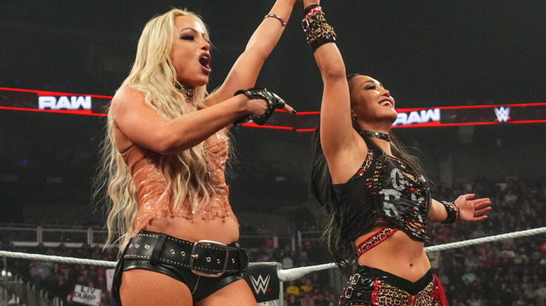 Liv Morgan holds Roxanne Perez's hand up and points at her following a victory.