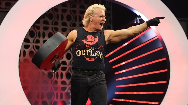 Jeff Jarrett pointing toward the audience while holding his guitar during his entrance at an AEW show.