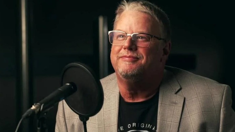 WWE backstage official Bruce Prichard smiles for a camera as he poses behind a microphone to announce the launch of his podcast.