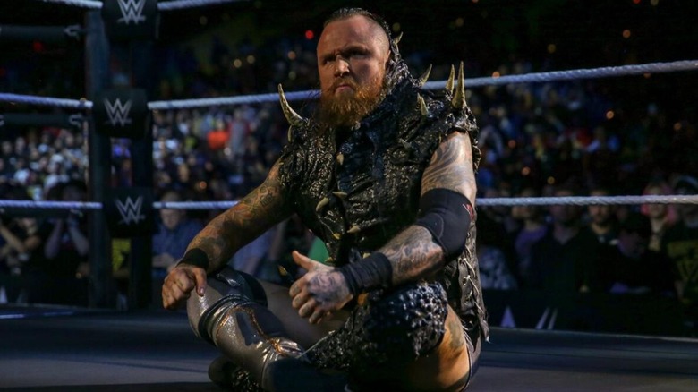 Aleister Black sits cross-legged in the ring during his entrance on an episode of WWE TV.
