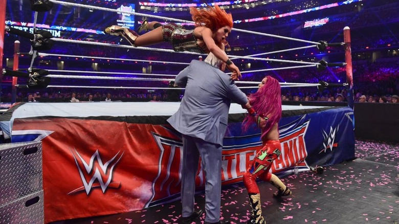 Becky Lynch looks to hit a suicide dive to Sasha Banks, who moves Ric Flair in front of the way, during their match at WrestleMania 32.