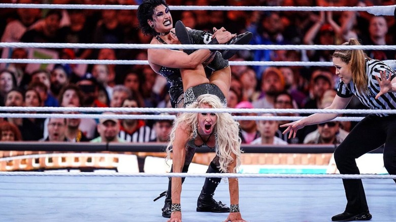 Rhea Ripley puts Charlotte Flair in a submission hold in the middle of the ring as the referee looks on during their match at WrestleMania 39.