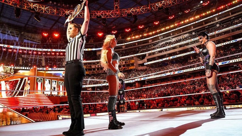 Rhea Ripley waves to Charlotte Flair, behind the referee's back as she holds up the SmackDown Women's Championship, ahead of their match at WrestleMania 39.