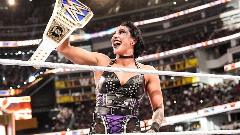 Rhea Ripley holds up the SmackDown Women's Championship and smiles in the ring after defeating Charlotte Flair at  WrestleMania 39.