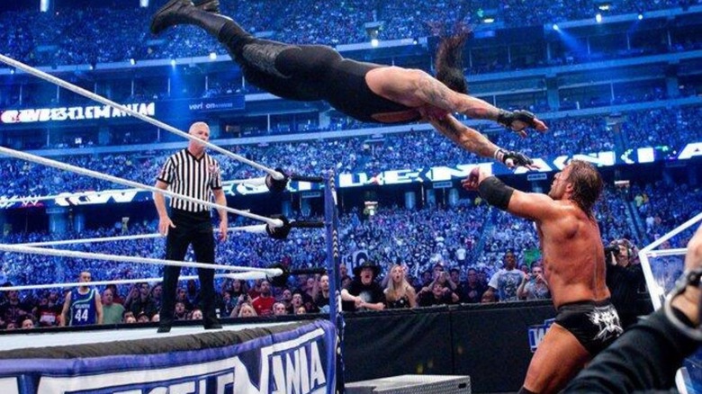 Undertaker hits a dive over the ropes to Triple H standing on the floor below during their match at WrestleMania 27.
