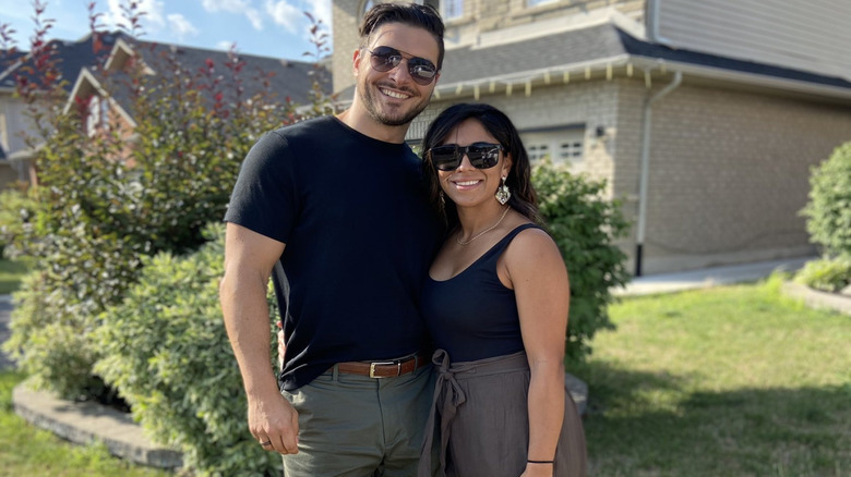 Ethan Page and his wife smile for the camera in front of a home in a photo posted to his X account.