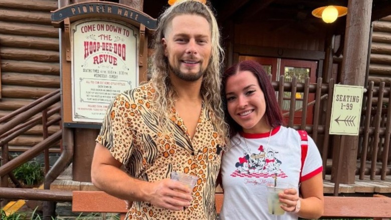 Lexis King and his girlfriend, drinks in hand, pose smiling in front of the Hoopty Doo Musical Revue at Walt Disney World.