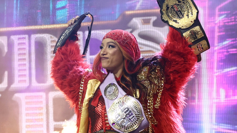 Mercedes Mone holds up two of her championships while wearing the others on the stage before walking down to the ring for a match on 