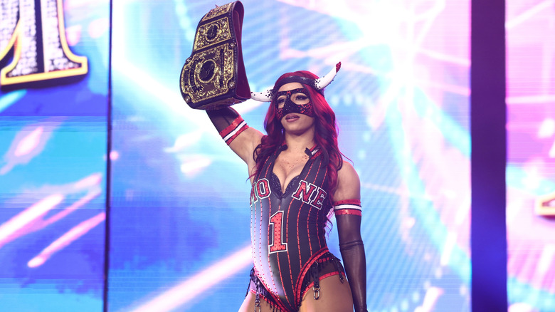 AEW Women's World Champion Mercedes Mone poses on the stage, her title held high, and looks toward the ring at AEW All Out 2026.