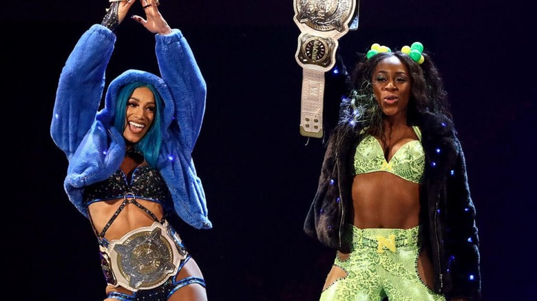 Sasha Banks and Naomi pose with their WWE Women's Tag Team Championships on the stage before a match.