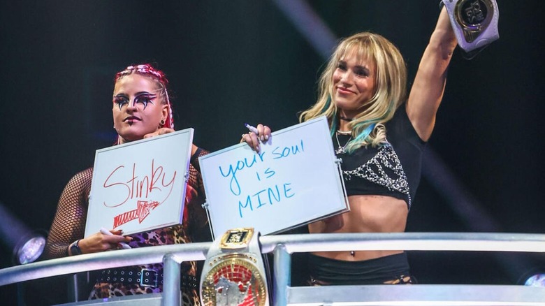 Zaria holds up a sign toward Sol Ruca that says "stinky," with Ruca holding one toward the ring that says, "Your soul is mine," during an episode of "WWE NXT."