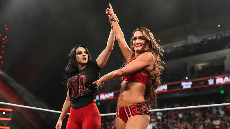 Stephanie Vaquer holding up Nikki Bella's arm with Bella pointing to Vaquer