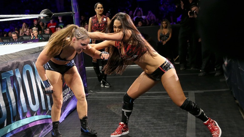 Ronda Rousey and Nikki Bella clashing at Evolution 2018 while Brie Bella watches on from ringside.