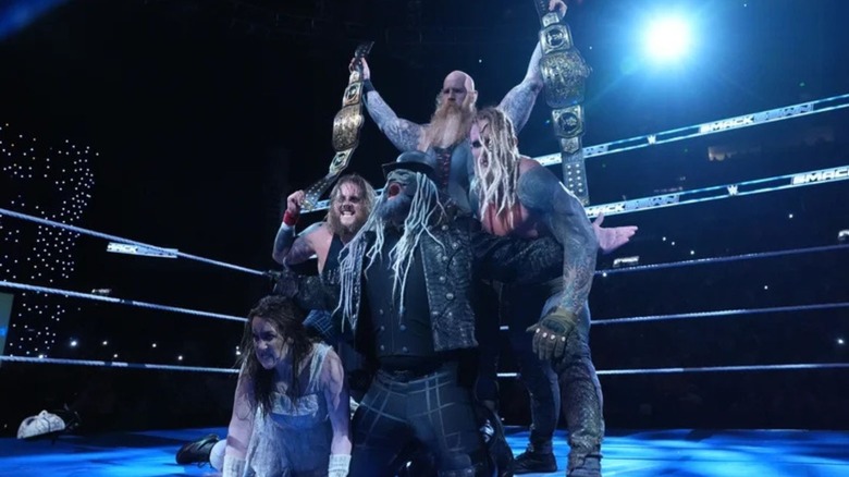 Erick Rowan holds up the WWE Tag Team Championships, as the rest of the Wyatt Sicks, including Joe Gacy, Dexter Lumis, Nikki Cross, and Uncle Howdy, pose in the ring before a segment on 