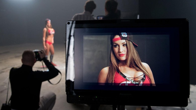 Nikki Bella posa detrás del escenario para una sesión de fotos de WWE.com, y la lente de la cámara se encuentra en el primer plano de la imagen.