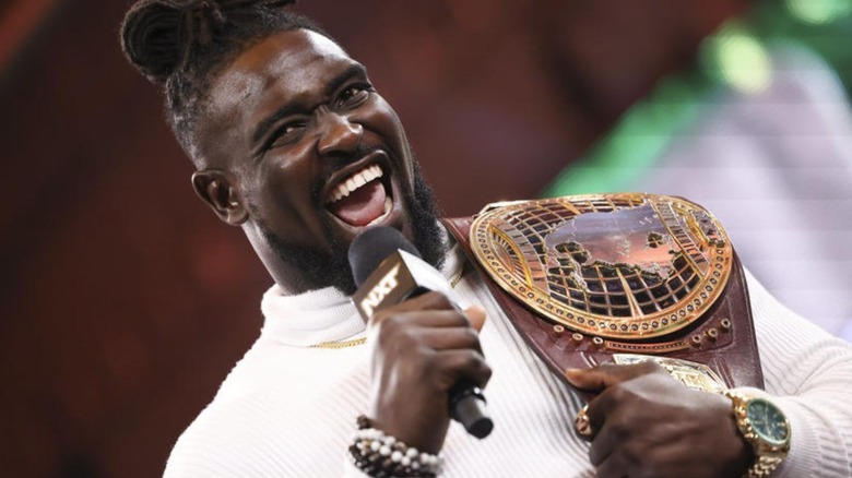 Oba Femi holds up his newly-won "WWE NXT" North American Championship while cutting a promo in the ring.