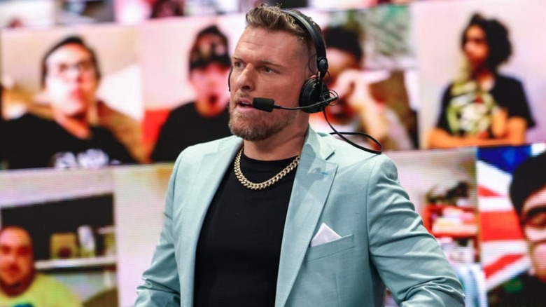 Pat McAfee is pictured ringside at the WWE commentary desk, wearing a headset.