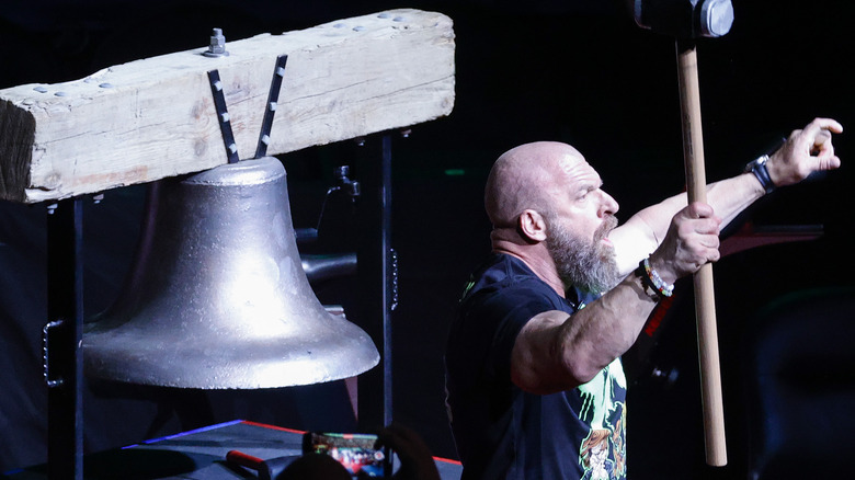 Triple H holding slegehammer next to bell