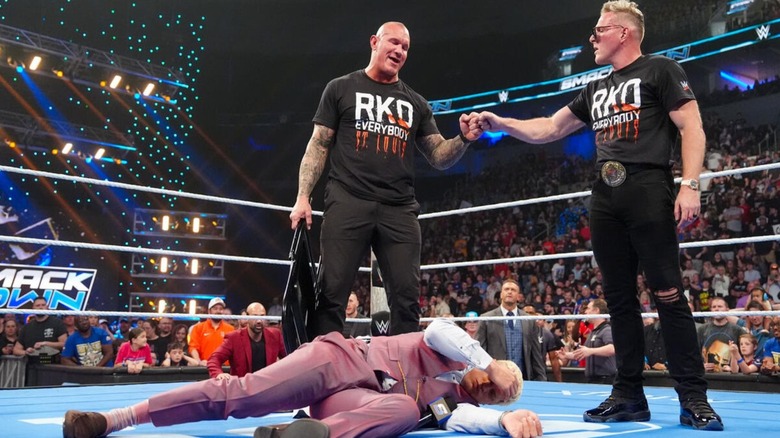 Randy Orton and Pat McAfee fist bump over a fallen Cody Rhodes in the ring on an episode of 